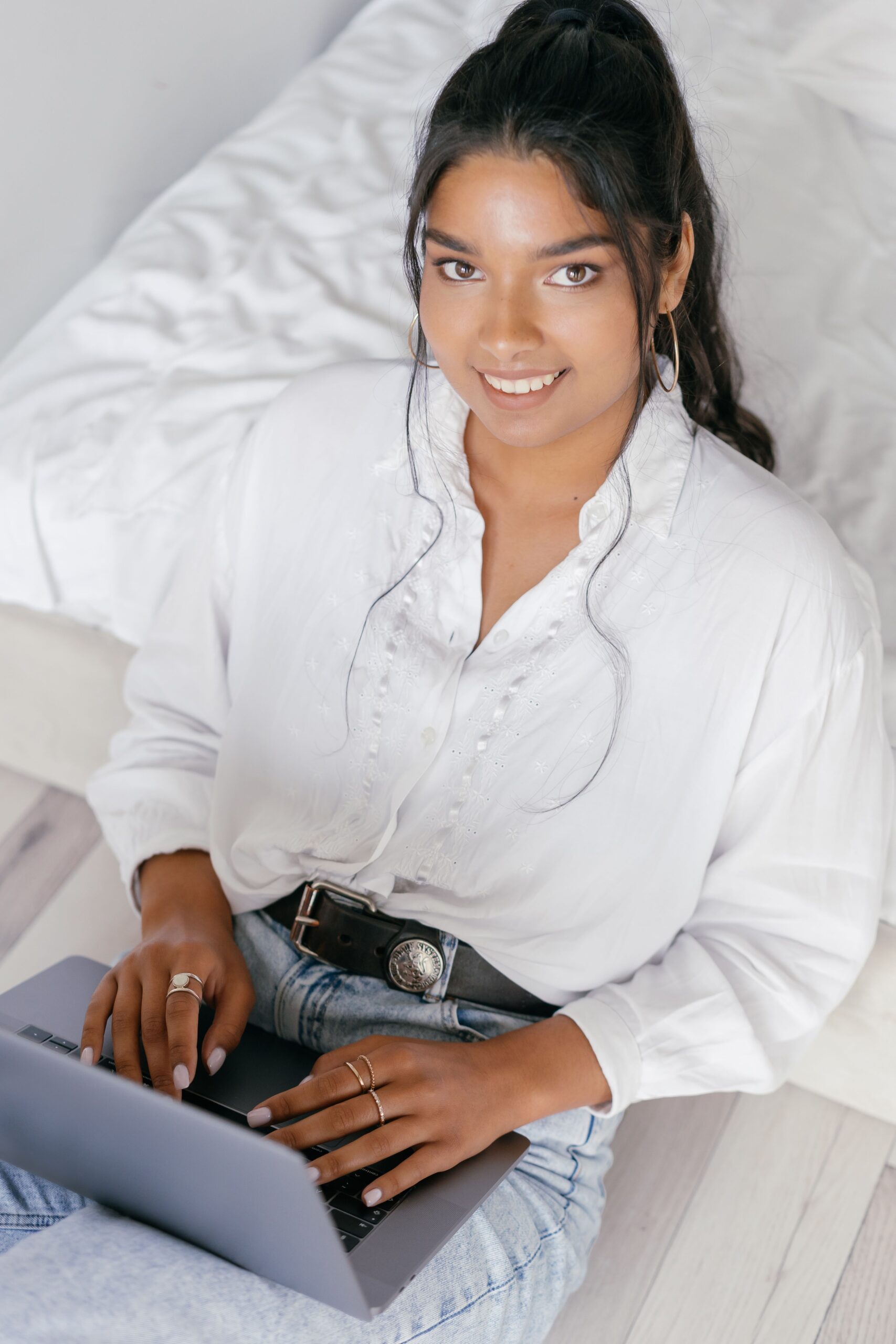 Smiling young woman typing on a laptop indoors, top view angle.